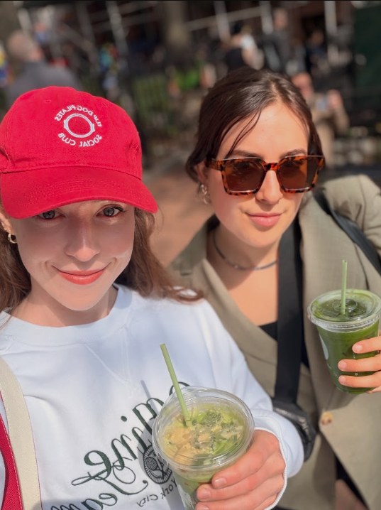 Two friends smiling in the sunshine holding iced matcha drinks.